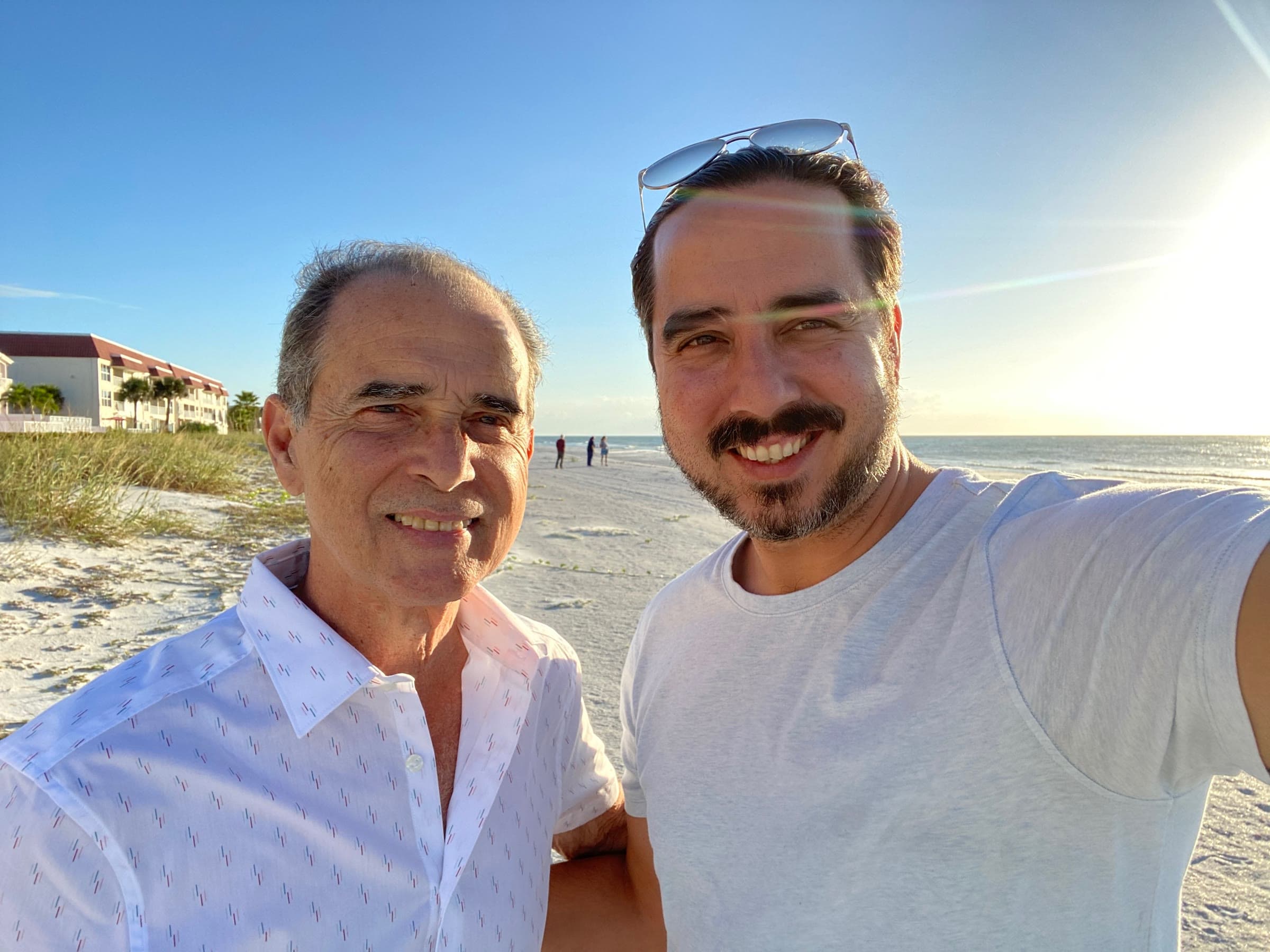 Manuel Suarez and his father Frank Suarez side by side on a beach at golden hour, both smiling, the sea behind them