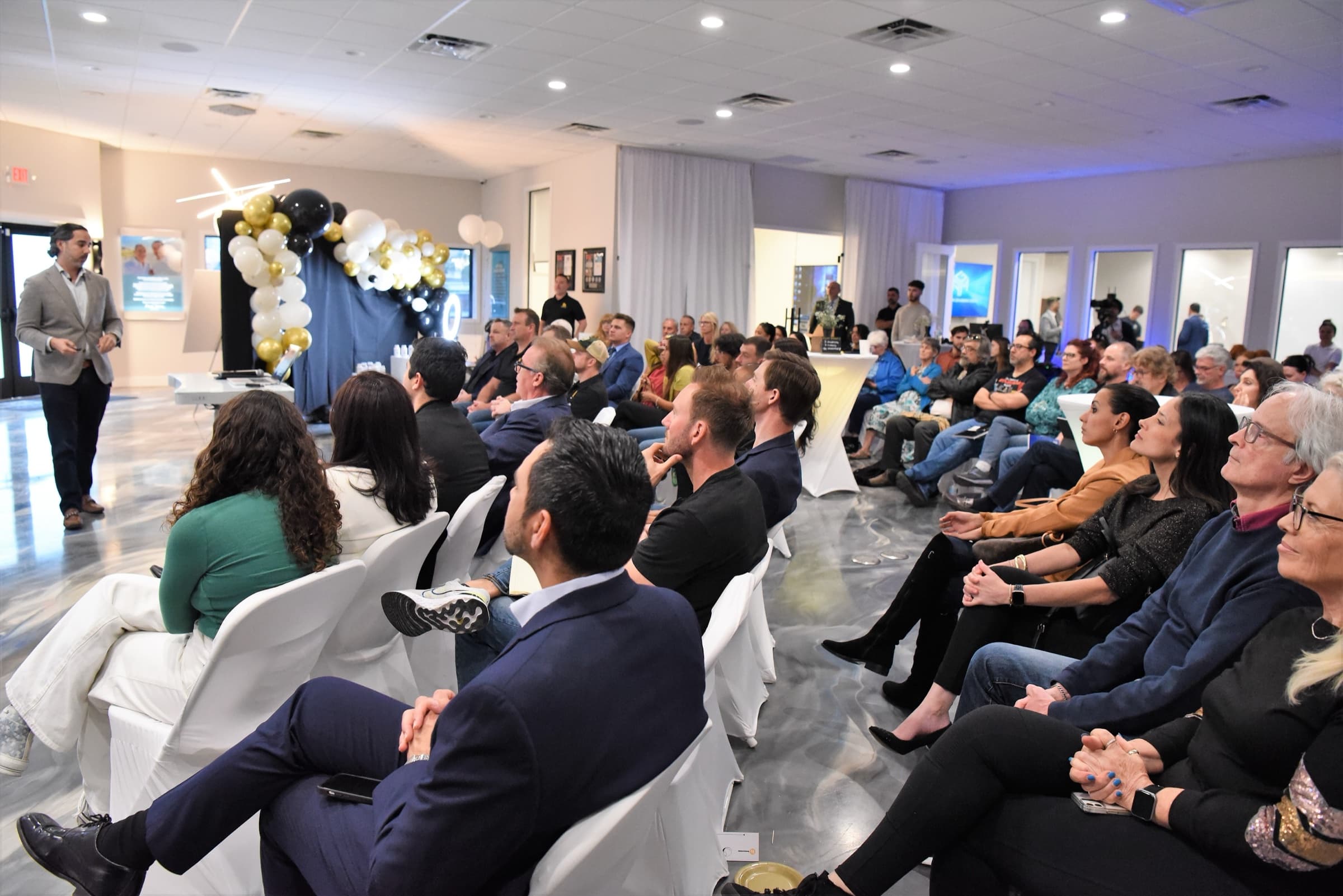 A full room of seated attendees turned toward Manuel Suarez as he speaks from the front of the AGM studio in Largo, Florida.