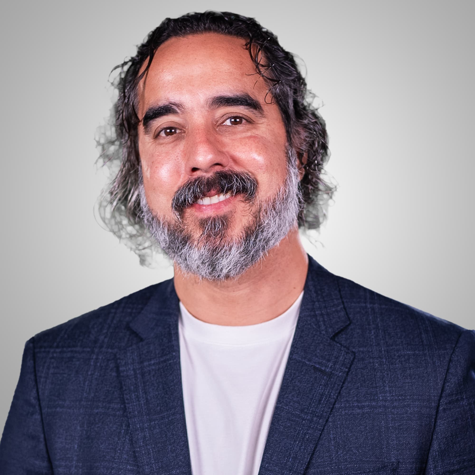 Manuel Suarez, studio headshot, navy blazer on a grey background