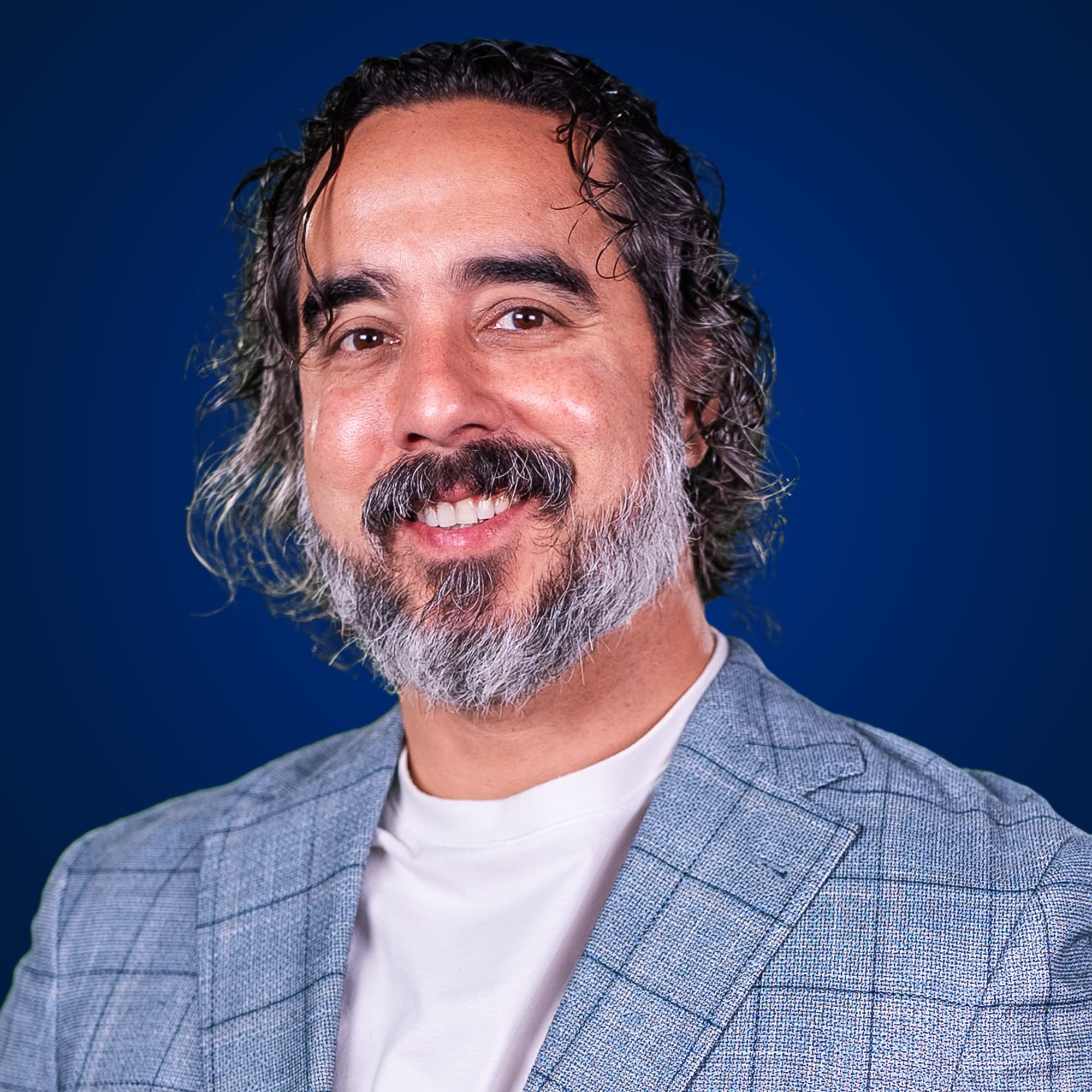 Manuel Suarez, studio headshot, light blue blazer on a deep blue background