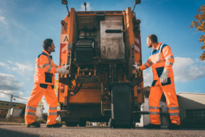 Two refuse collection workers loading garbage into waste truck emptying containers