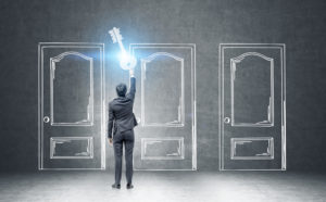 Rear view of a businessman in a dark suit holding a giant key standing near a black wall with three doors drawn with chalk. Concept of an opportunity. Toned image