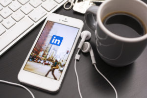 linkedin in cellphone and headset with a cup of coffee